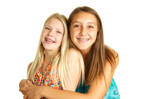 Sisters with braces, ages thirteen and ten smiling on a white background