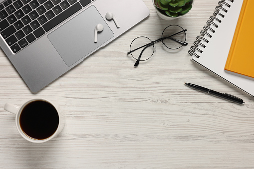 Flat lay composition with laptop and different stationery on white wooden desk, space for text. Home office