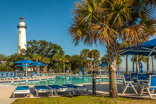 St. Simons Lighthouse and Pool The St. Simons Lighthouse stands tall behind the public swimming pool at Neptune Park in the Village area of St. Simons Island, GA saint simons island photos stock pictures, royalty-free photos & images