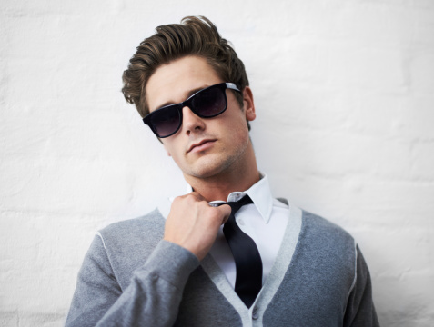 A trendy young man loosening his tie while leaning against a wall