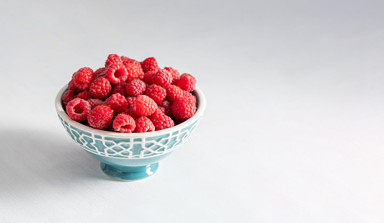 fresh raspberries in a blue bowl at the white table, summer harvest fruits and fresh berries, vitamins, vegetarian concept, High quality photo