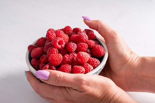 Kid's hands hold a full jar of fresh raspberries ready ti eat on a summer day in the garden.