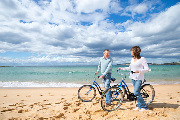 couple d'âge mûr à vélo sur la plage - senior couple cycling beach bicycle photos et images de collection