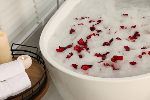 Bath tub with foam and red rose petals in bathroom