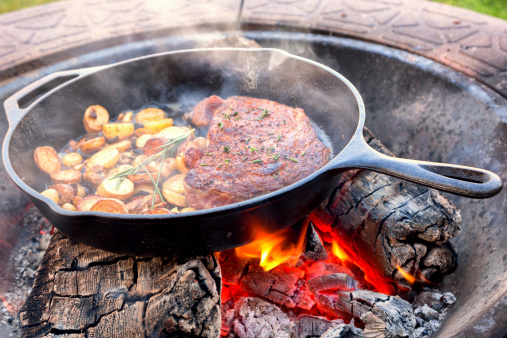 Rib eye steak and potatoes cooking on a campfire outsideRib eye steak and potatoes cooking on a campfire outside