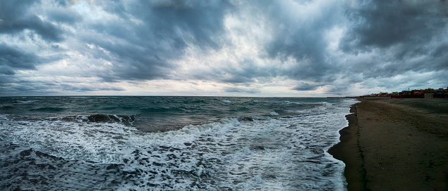 Awesome panoramic 180 degrees of rough sea at sunset on blue hour at  beach, a dramatic sky with amazing light and cloudscape and sun reflections with on water edge crashing with foam.