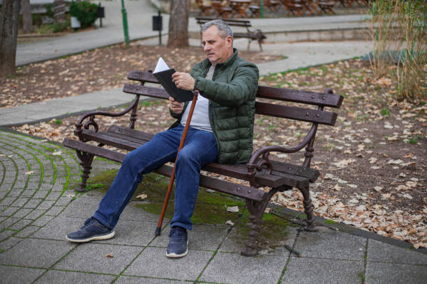 istock An elderly man sits on a bench in a public park and reads a book 1870578880