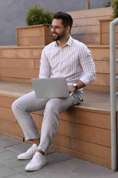 istock Handsome young man using laptop on bench outdoors 1870607193