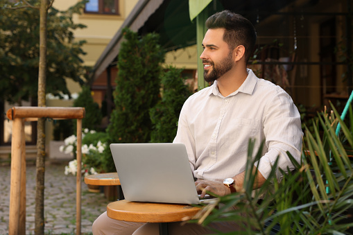 Handsome young man working on laptop at table in outdoor cafe