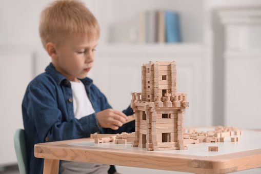 Cute little boy playing with wooden tower at table indoors, selective focus. Child's toy