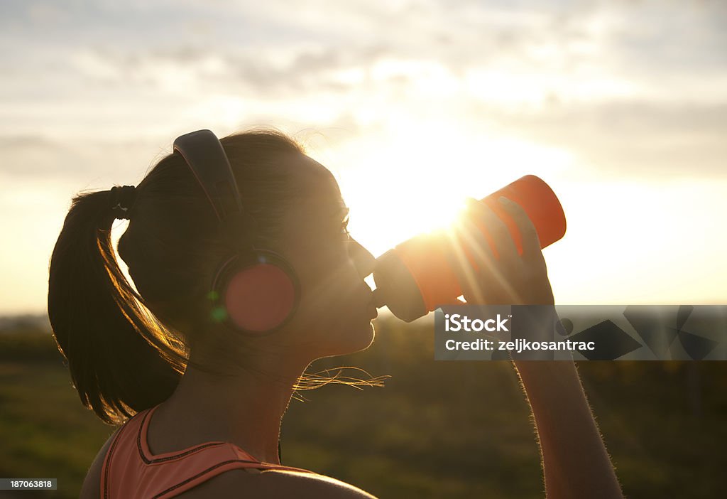 Женщина питьевой воды на закате - Стоковые фото Бутылка роялти-фри