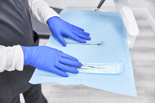 From above of crop anonymous doctor in medical gloves and uniform preparing mouth mirror and various dental tools for examining teeth in modern clinic