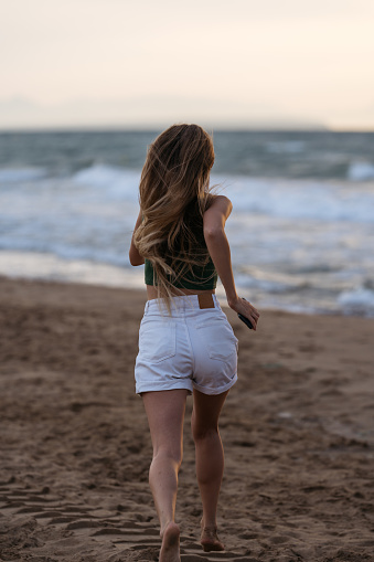 Back view of slim woman with long blonde hair running towards sea.