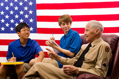 Two teenage boys interview a local Army veteran for a school project on Veteran's Day, USA.