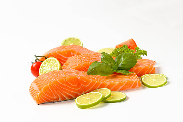 salmon fillets three raw salmon fillets with garnish isolated on white background lime basil plant stock pictures, royalty-free photos & images