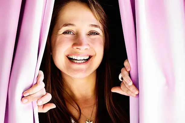 Peeping out through closed pink drapes, this pretty blonde woman smiles joyfully  at someone she's obviously very happy to see!
