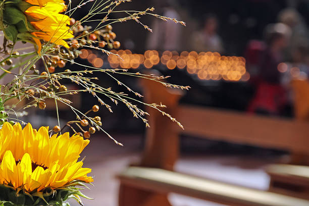 Bokeh lights and sunfowers in a church. Focus on the sunflowers. unrecognizable people in the background burning a votive candle.