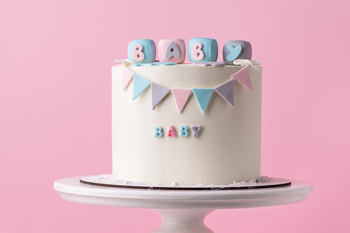 Baby shower party cake with white chocolate frosting. Guess the gender of the upcoming child. He or She cake. Reveal the gender of the unborn baby. Blue or pink sponge bisquit inside. Pink background