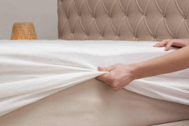 istock Changing bed sheets. Woman is putting on a fitted white cotton sheet on a mattress while making the bed. 1870713040
