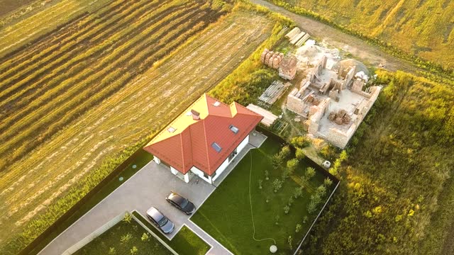 Top down aerial view of two private houses, one under construction with wooden roofing frame and another finished with red tiled roof