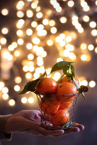 mandarini in un secchio a rete su una mano maschile su uno sfondo di bokeh luminoso - defocused illuminated glitter orange foto e immagini stock