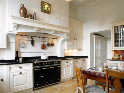 Stylish kitchen with large gas stove and cabinets. White ceramic tiles under exhaust.