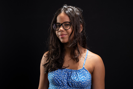 Beautiful brunette woman in glasses looking at camera wearing blue outfit against black background.