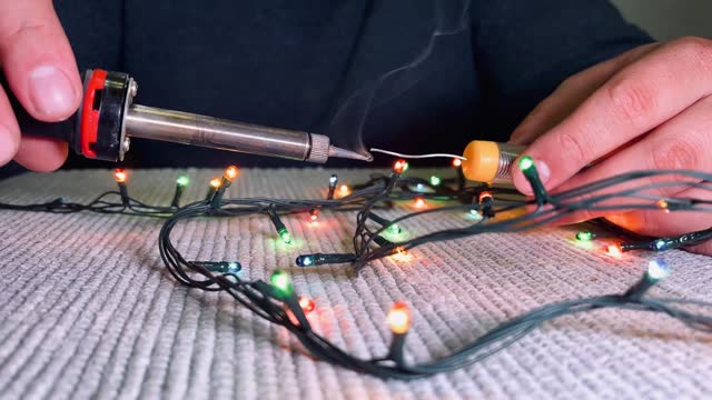 Soldering iron in a man's hand. Male hands close-up repairing an electric garland.