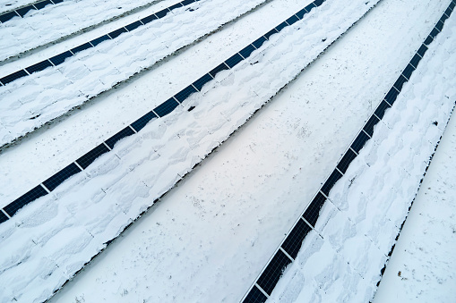 Aerial view of snow covered sustainable electric power plant with rows of solar photovoltaic panels for producing clean electrical energy. Low effectivity of renewable electricity in northern winter.