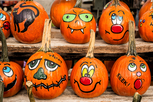 A group of pumpkins hand painted with faces for halloween sitting on a shelf