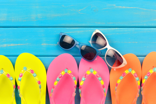 Colored thongs and sunglasses on a blue decking background with copy space