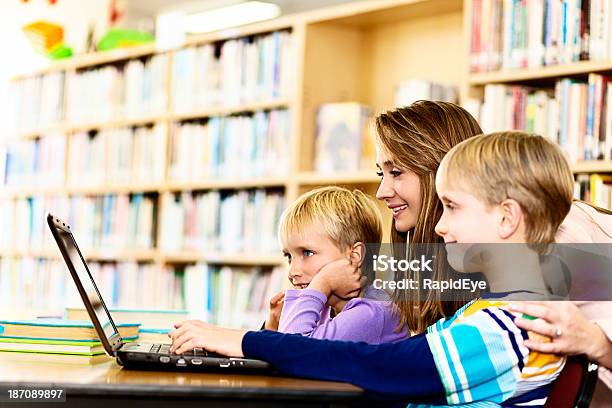 Photo libre de droit de Femme Souriante Aide Les Enfants Avec Un Ordinateur Portable Dans La Bibliothèque banque d'images et plus d'images libres de droit de 10-11 ans