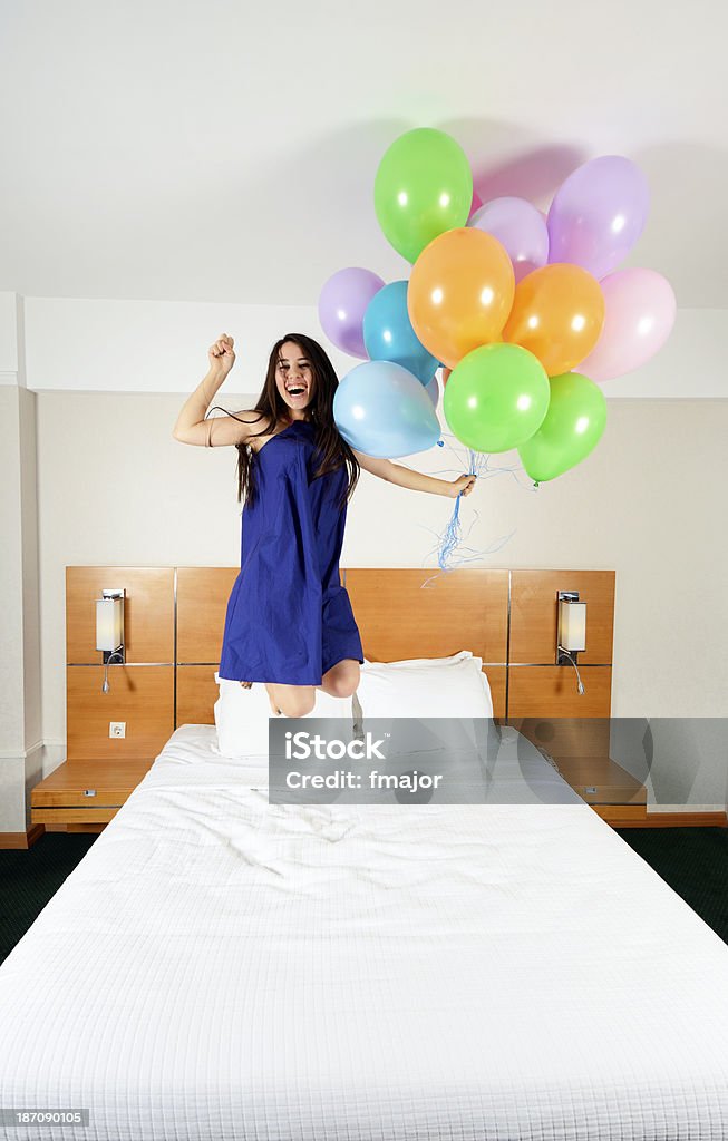 Vitality Young girl is jumping with flying balloons on the bed. Adult Stock Photo