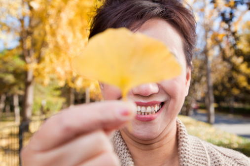 Mature Woman Covering Her Eyes with Yellow Ginkgo Leaf