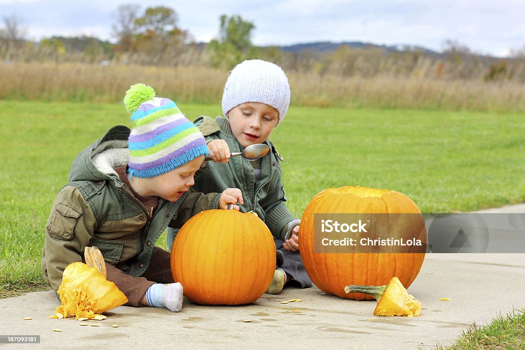 Two Young Children Carving Pumpkins Two little boys are sitting outside on a fall day before halloween, carving jack-o-lantern pumpkins 12-17 Months Stock Photo