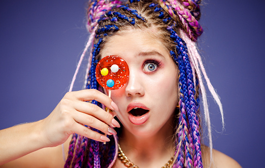 Young pretty woman with dreadlocks hairstyle and creative make-up in doll style with candy