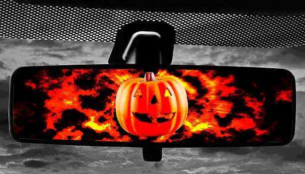 Jack-O-Lantern on fire reflected in rearviewmirror of a car