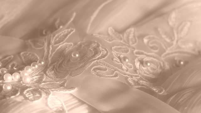 Close up of wedding dress lace and fabric with beads and pearls, soft light,
