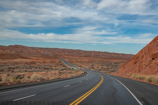 Highway through tall spires and mesas of rich dark red rugged mountains near Monument Valley in Arizona and Utah of western USA in North America. This is part of the Navajo Indian Nation in USA.  Nearest cities are Phoenix, Arizona, Salt Lake City, Utah, Denver and Durango, Colorado.