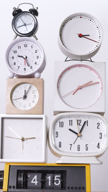 Many clocks turning to tell the time on a white background.