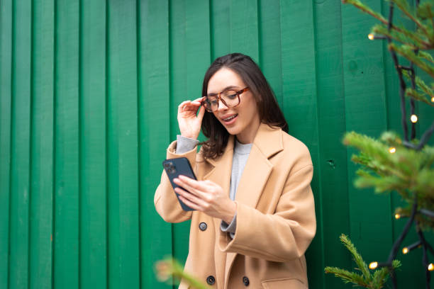 istock Close up smiling woman using smartphone, standing near Christmas tree 1871012666
