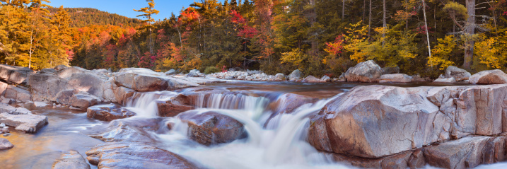 Multi-coloured fall foliage along the Swift River Lower Falls, White Mountains National Forest in New Hampshire, USA. A seamlessly stitched panoramic image.