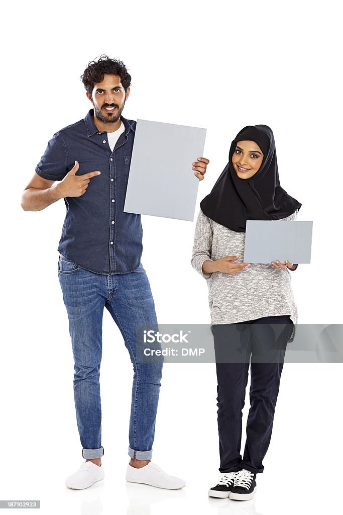 Attractive young couple showing blank billboards Full length portrait of attractive young couple showing you blank billboards over white background Asian and Indian Ethnicities Stock Photo