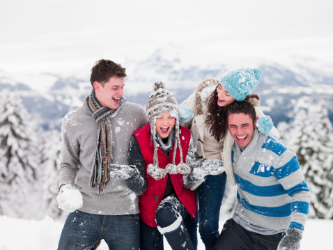 Four young adults close together on a mountain with snow in their hands