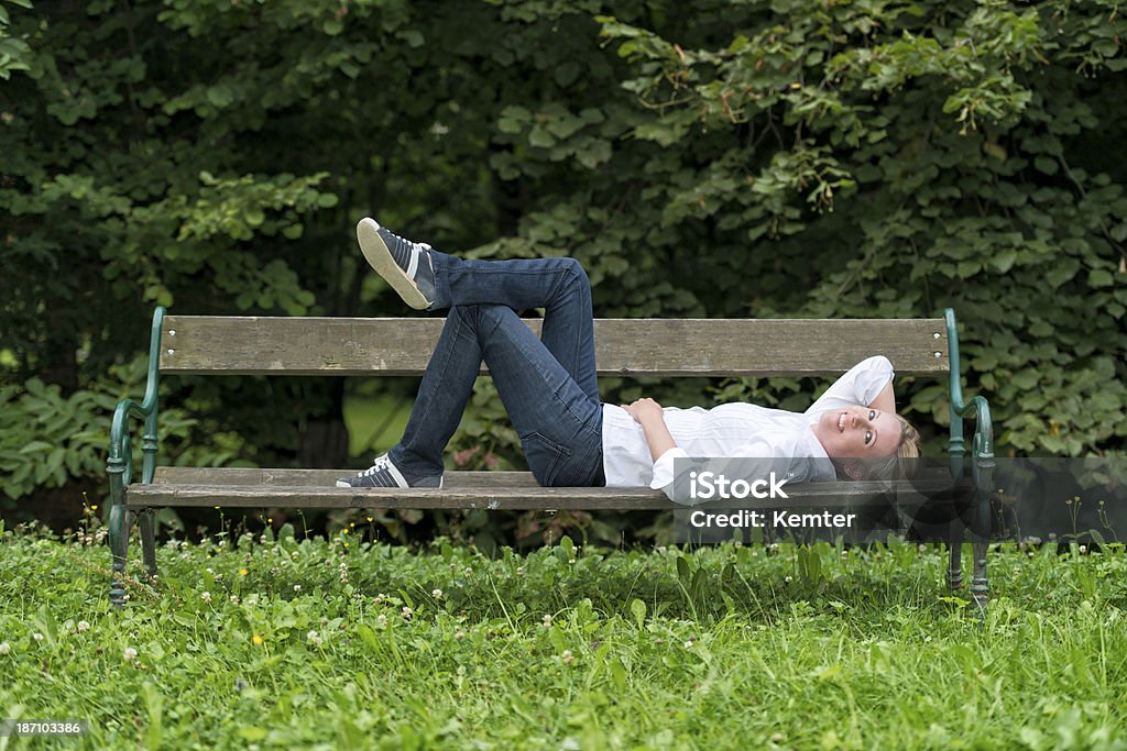 Attraente donna bionda mette Sdraiato su un parco bench - Foto stock royalty-free di Abbigliamento casual