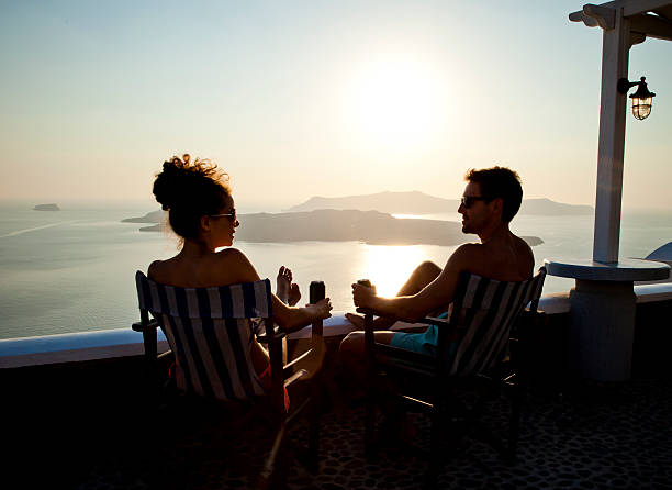 Santorini Sunset Silhouette of a young couple enjoying a sunset with a drink. Santorini, Greece. happy couple on vacation in santorini greece stock pictures, royalty-free photos & images