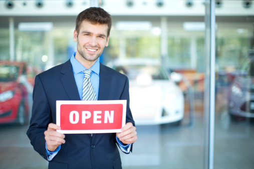 Young men, car dealership owner or manager holding OPEN sign while standing in salon.
