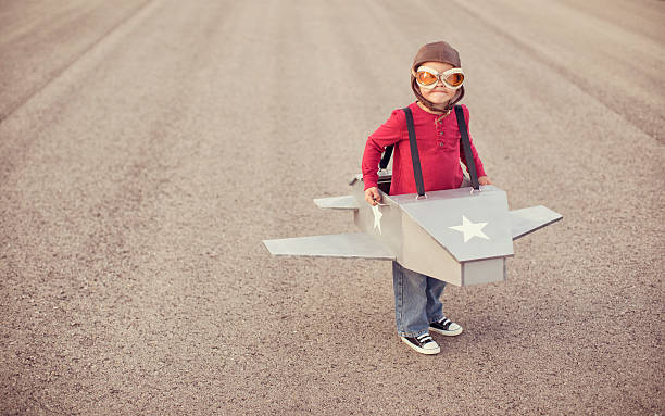 Young boy flying a cardboard airplane A little boy dreams of growing up and flying his own airplane. upward mobility stock pictures, royalty-free photos & images