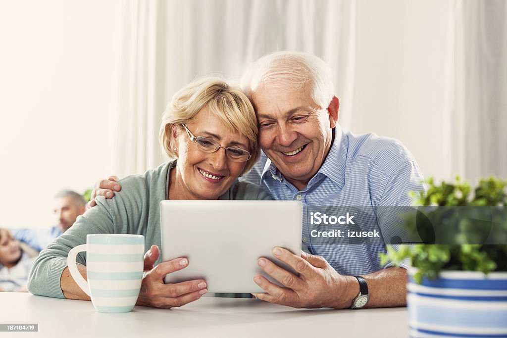 Senior couple with digital tablet Cheerful senior couple sitting by the table at home and using a digital tablet together. 60-69 Years Stock Photo