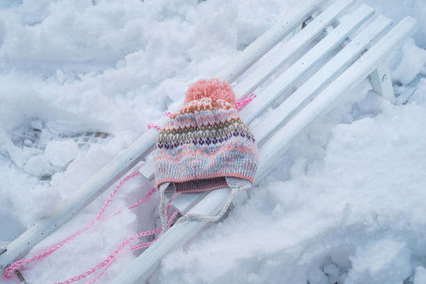 Discover the playful charm of winter with a white sled resting gracefully on the snow, adorned with a vibrant and colorful winter cap. This delightful scene captures the joy and vibrancy of winter adventures
